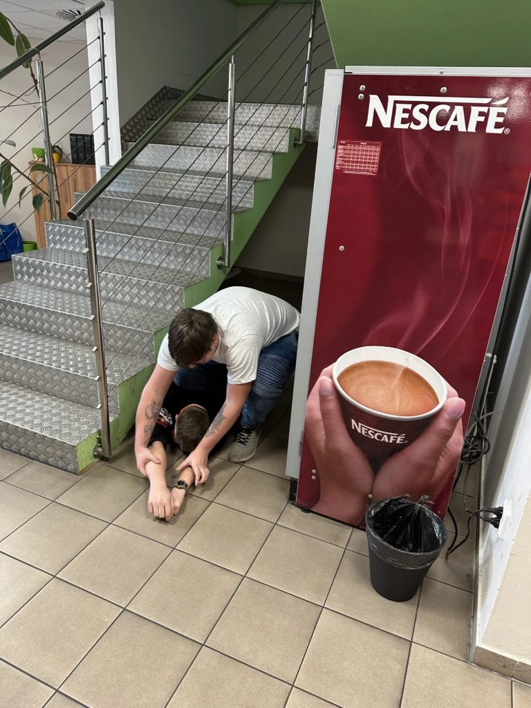 Muž poskytuje první pomoc člověku na schodech u kávomatova.